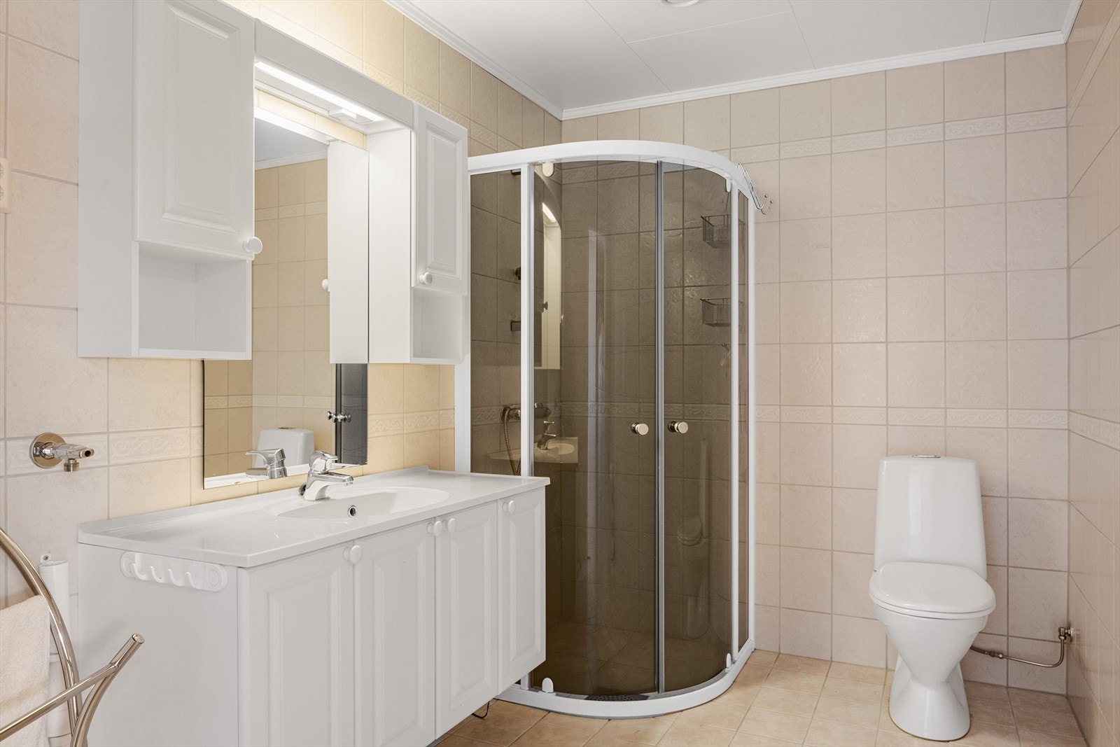 Badet har varmekabler i gulv og flislagte overflater. Åpen dusjløsning med glassdører mot rommet og gulvstående toalett. Galleribilde