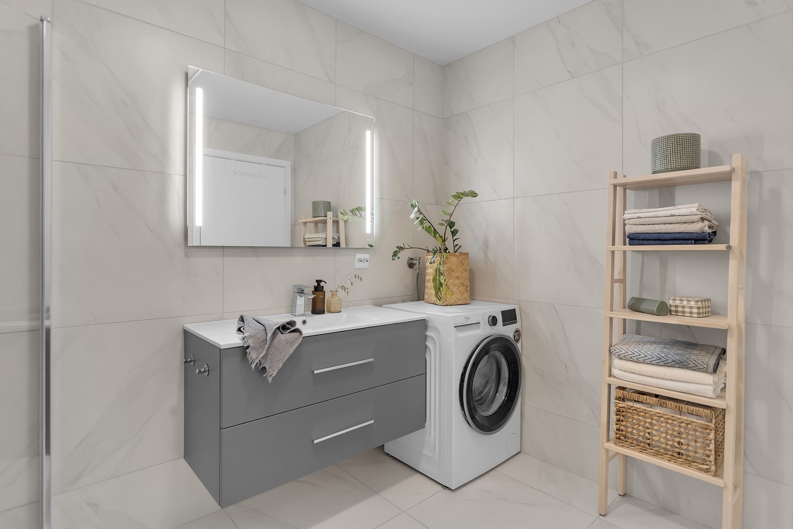 Rommet har i tillegg et praktisk speil med integrert belysning, en servant med underskuffer for effektiv oppbevaring samt et stilrent toalett. Gulv og vegger er kledd med elegante 60x60 fliser, vannbåren gulvvarme skaper en lun og behagelig atmosfære. Galleribilde