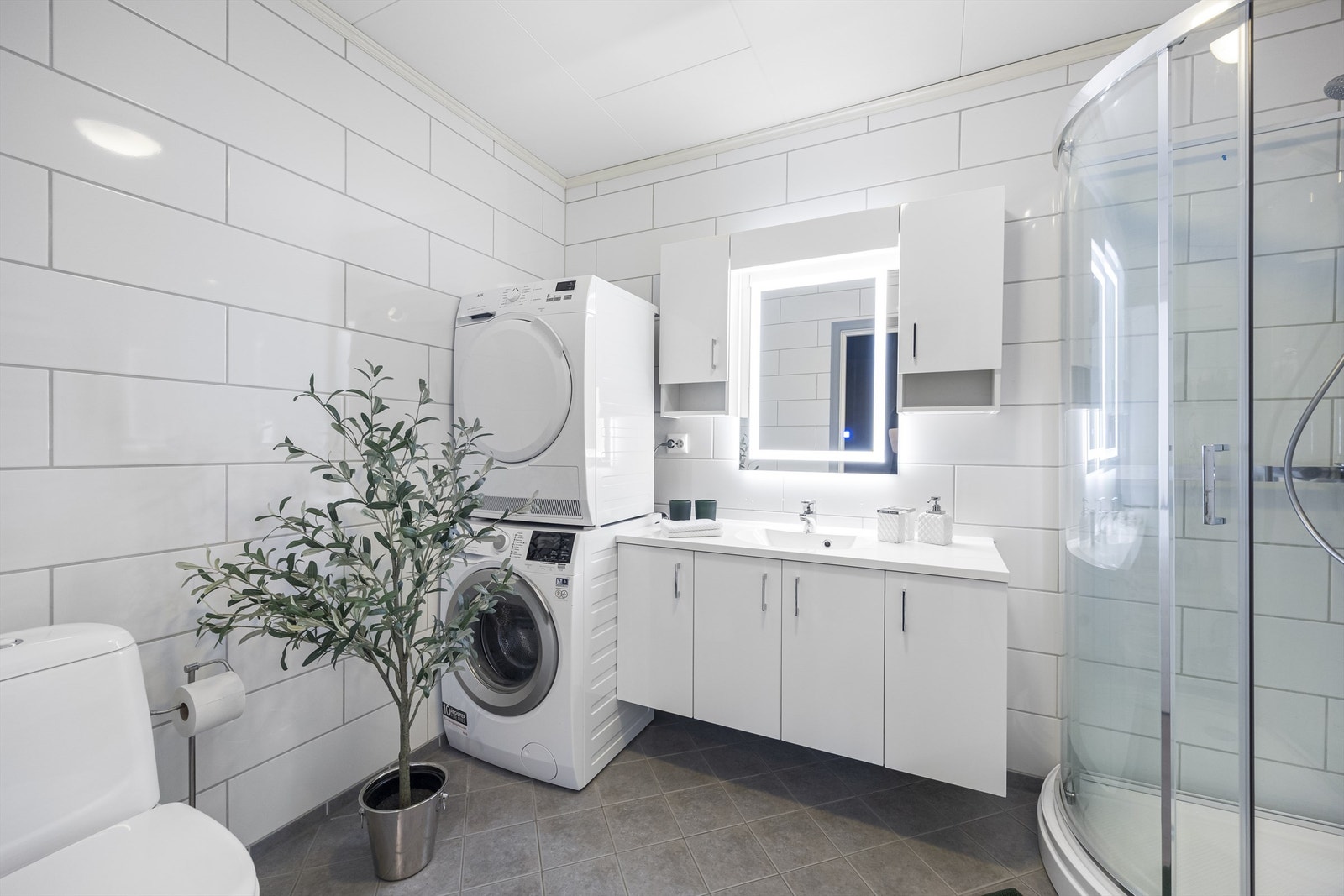 Badet er romslig og utstyrt med servantinnredning, dusjkabinett, toalett og opplegg for vaskemaskin. Galleribilde