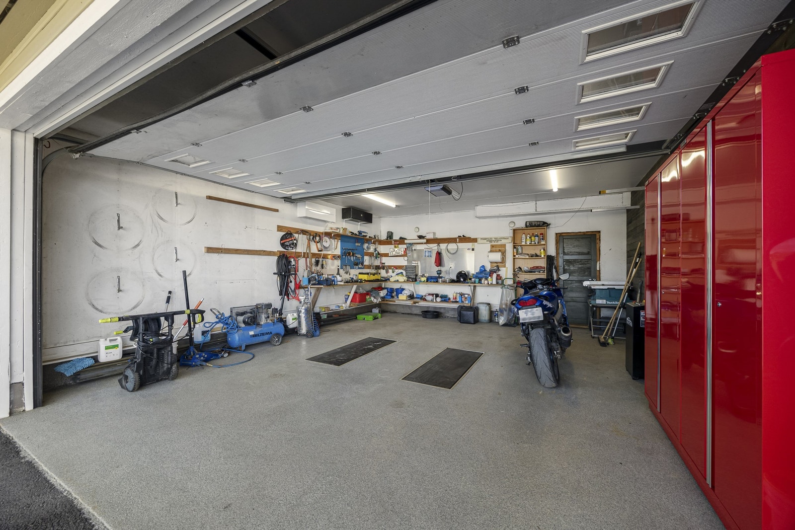 Stor garasje med gulvinnfelt løftebukk, varmepumpe og bod Galleribilde