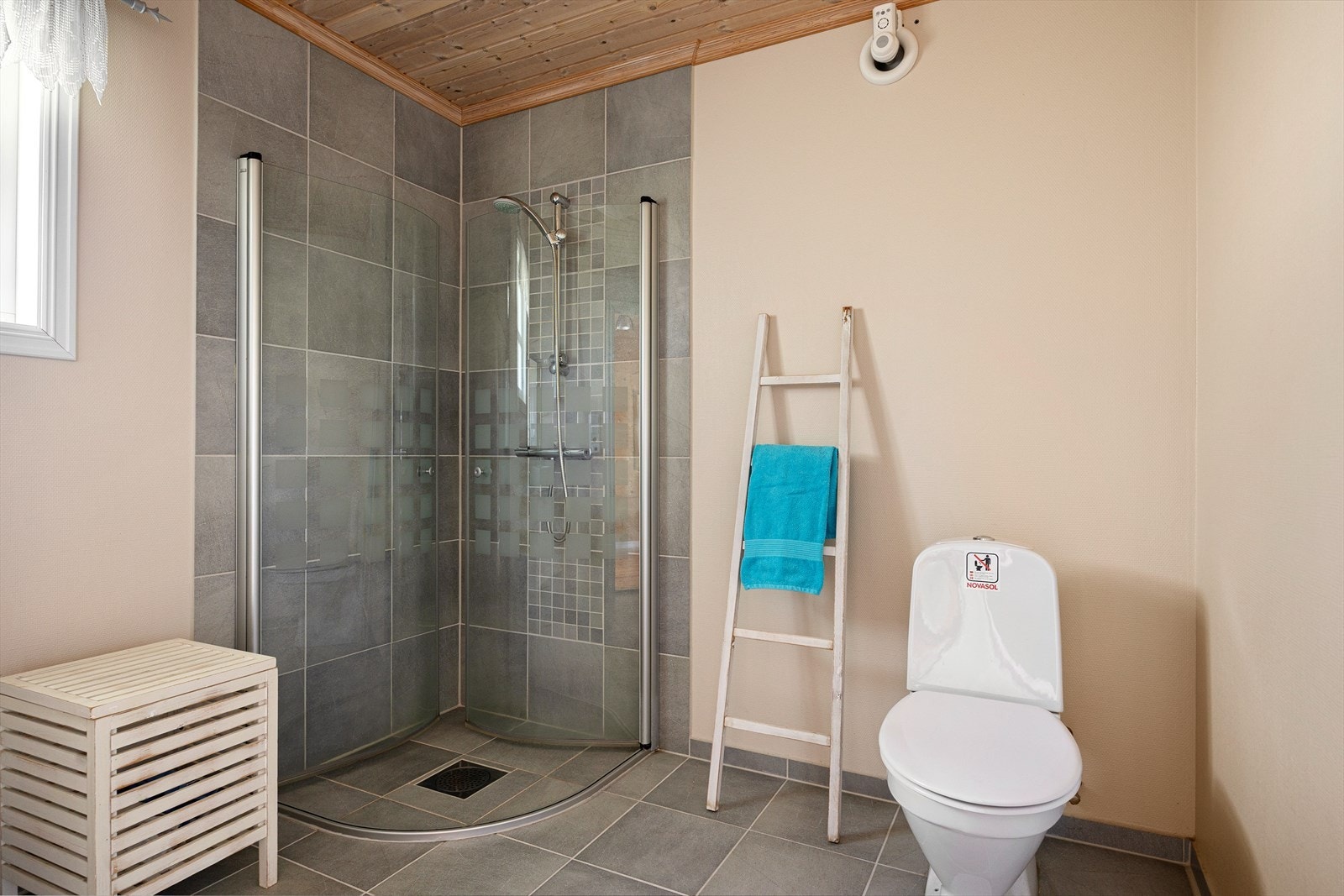 Badet har flislagt gulv med elektriske varmekabler, dusjhjørne og toalett. Galleribilde