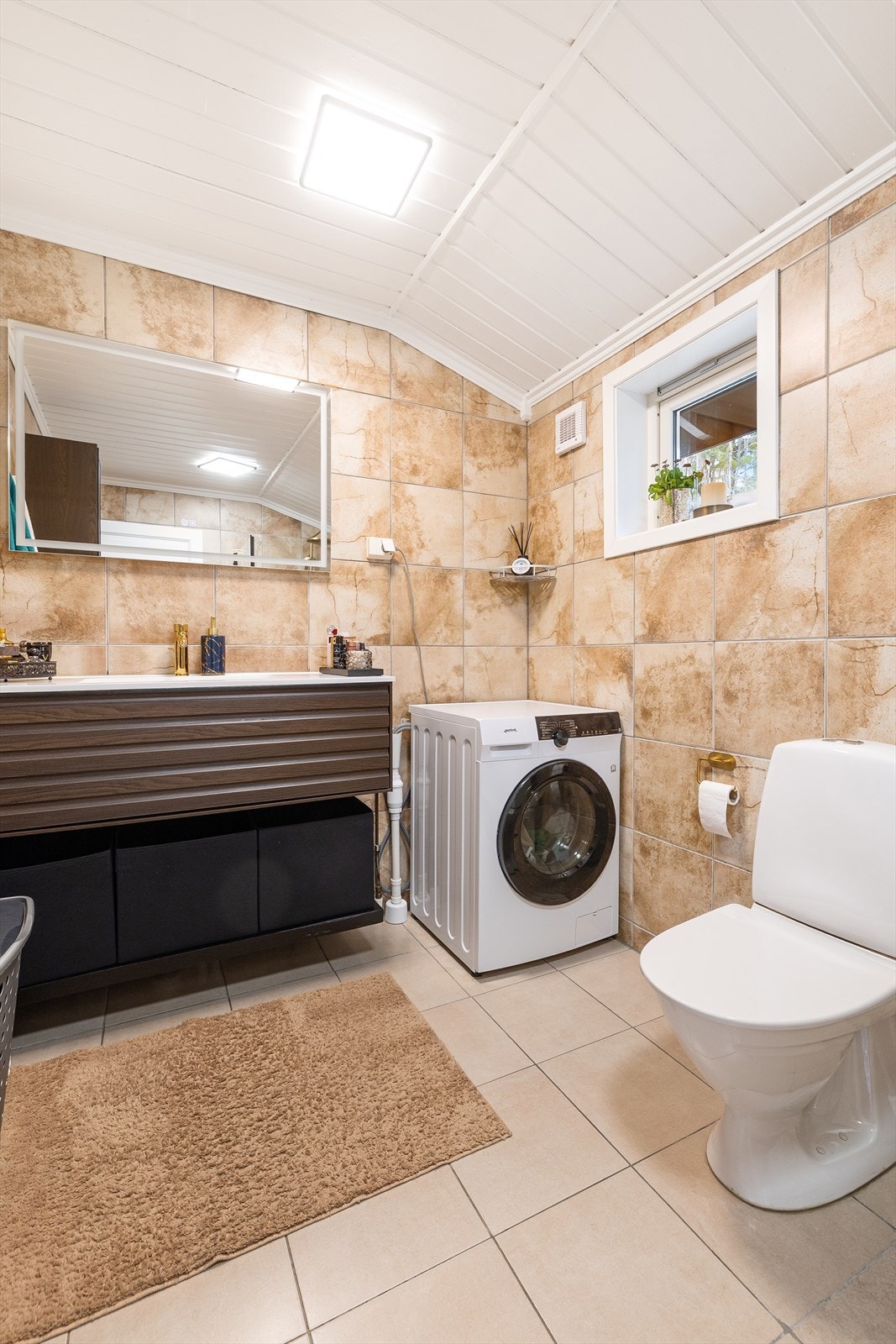Badet er innredet med toalett, servant i baderomsinnredning, speil med belysning, dusj og opplegg for vaskemaskin. Galleribilde