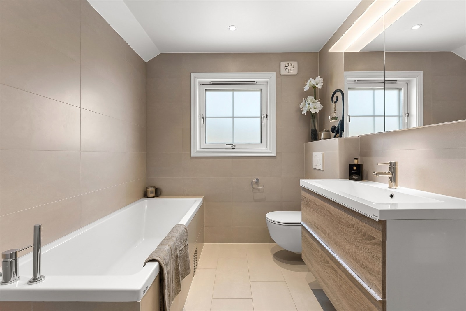 Pent baderom fra 2020 med fliser på gulv med gulvvarme, fliser på vegger og malt himling med downlights Galleribilde