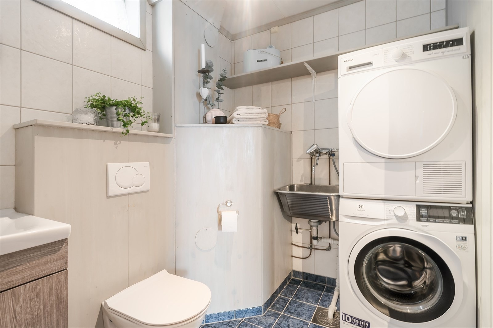 Badet i sokkeletasjen er praktisk innredet og har flislagte overflater på gulv og vegger. Rommet har servantinnredning, vegghengt toalett, badekar, utslagsvask og plass til vaskemaskin og tørketrommel. Galleribilde