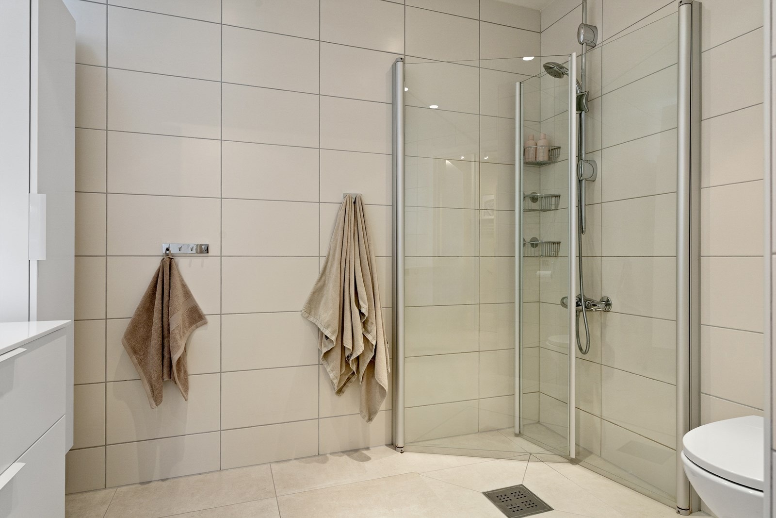 Videre er badet utstyrt med vegghengt toalett og dusjsone med innfelte dusjdører i herdet glass. Det er også opplegg for vaskemaskin. Galleribilde