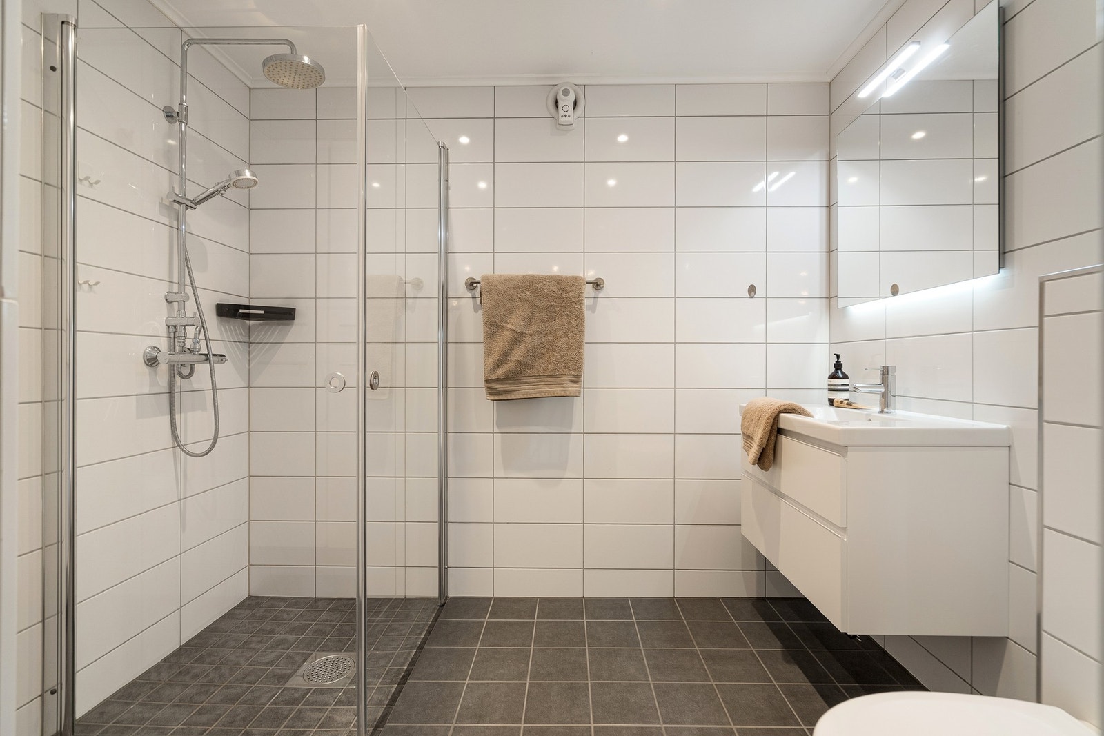 Badet har dusj i hjørne, vegghengt toalett og servant med underliggende skuffer Galleribilde