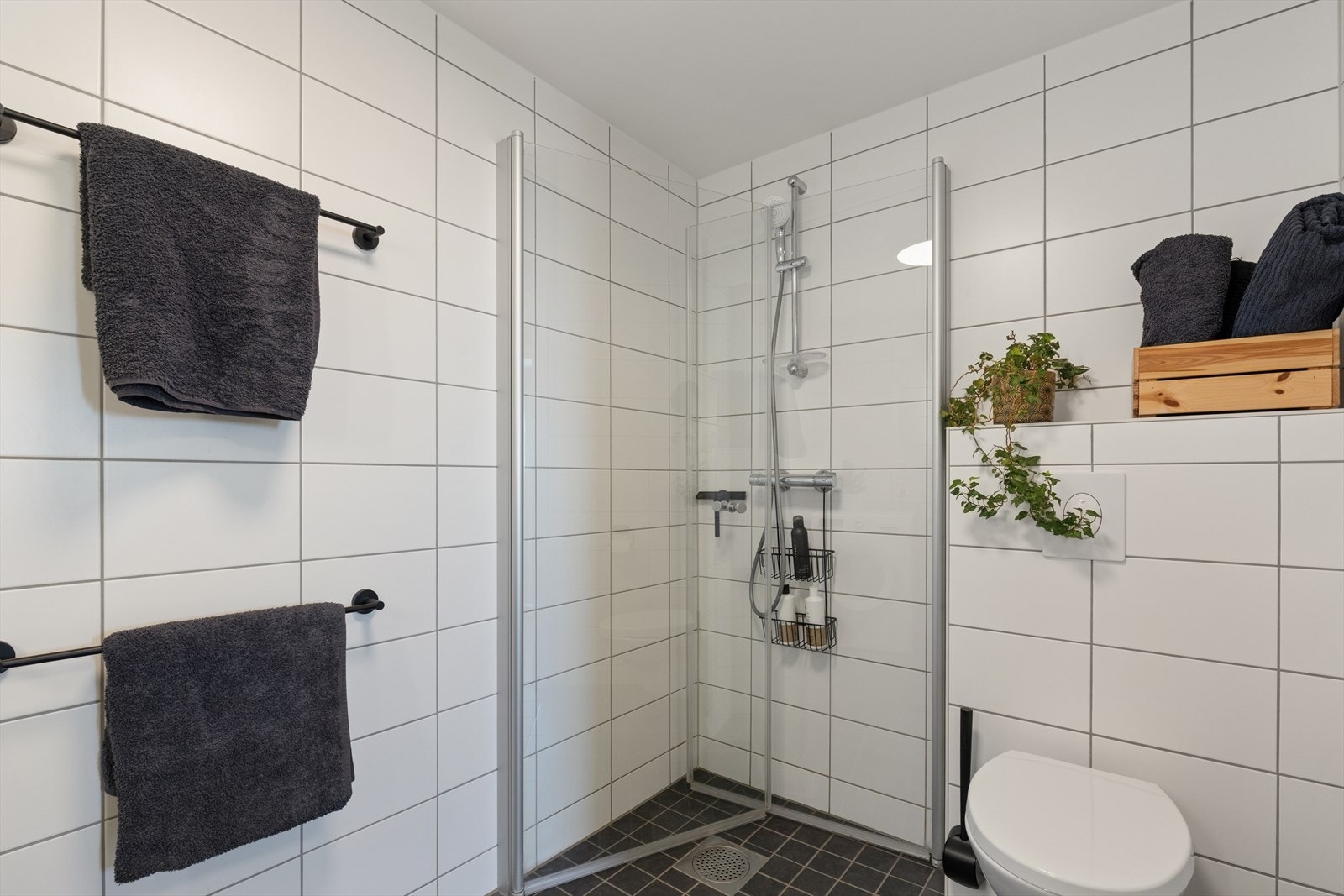 Badet er utstyrt med veggmontert toalett, dusjhjørne med innfellbare dører og en baderomsinnredning med servant og speil. Galleribilde