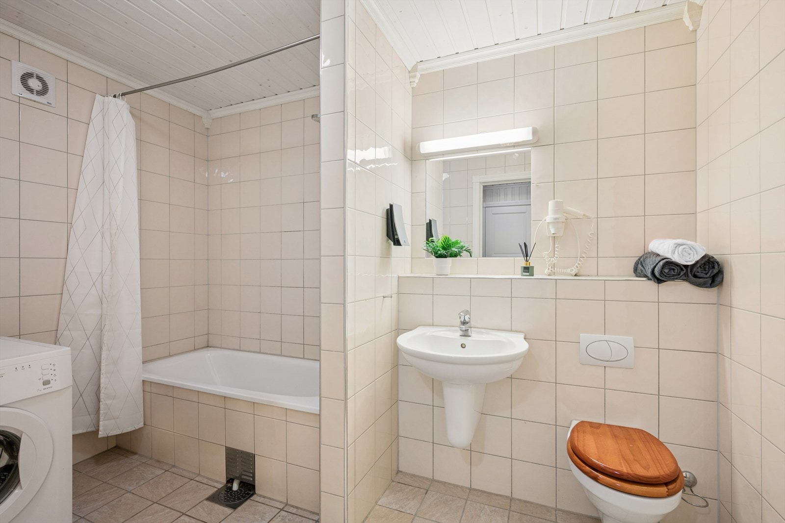 Bad i underetasjen med flislagte overflater, badekar og vegghengt toalett. Galleribilde