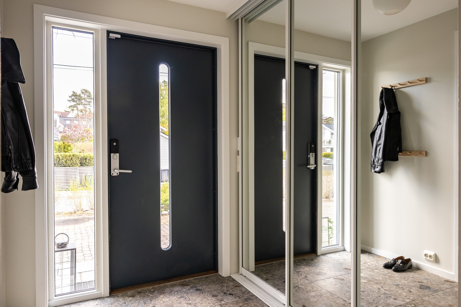 Entreen har store fliser på gulvet og varmekabler. Her kan du trille barnevognen inn ved behov. Ytterdøren har glassfelt, sidevindu og kodelås. En stor skyvedørsgarderobe med speilfronter gjør det enkelt å rydde unna yttertøy og sko. Galleribilde