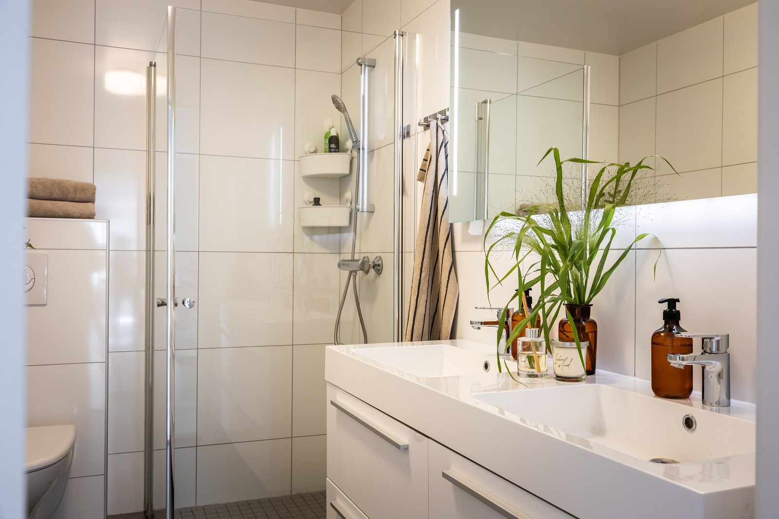 Dette badet er innredet med en heldekkende dobbeltservant på en skuffeseksjon, bredt speil med integrert belysning, et veggmontert toalett og et dusjhjørne med innfellbare glassdører. Galleribilde