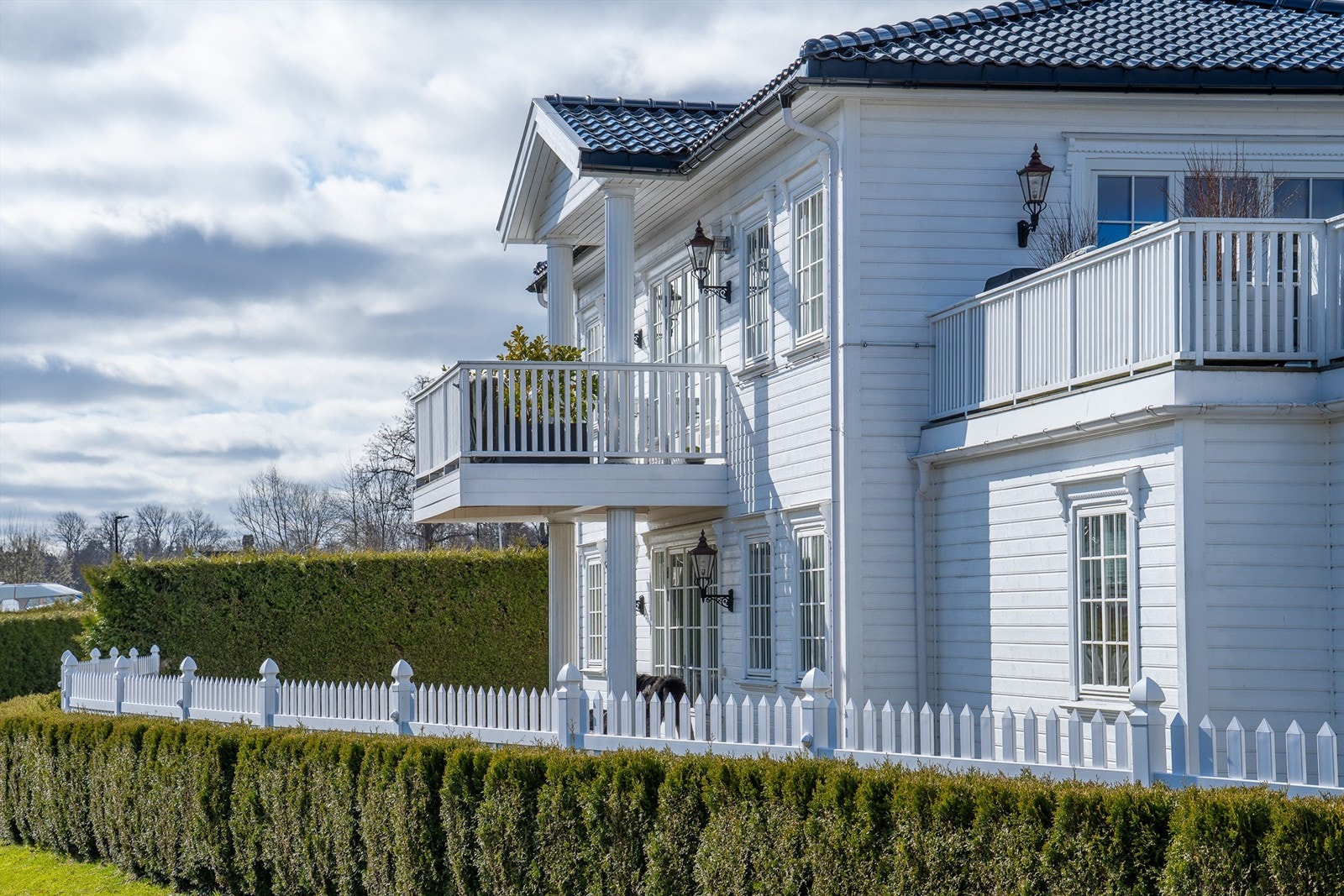Eiendommen fremstår med et stilrent uttrykk med utebelysning, søyler, glasert takstein og pent opparbeidet hage. Galleribilde