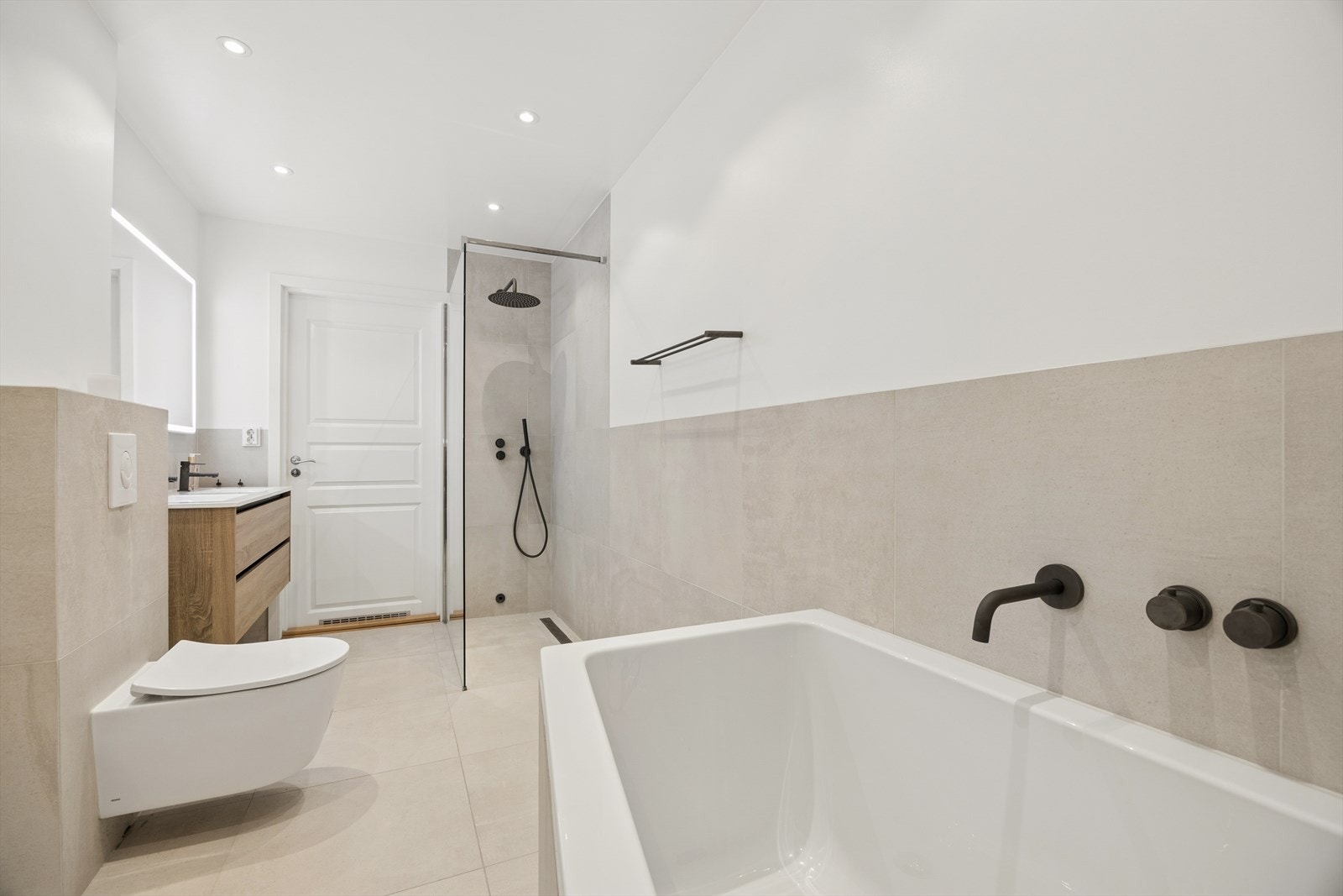 Badet har veggmontert dusjvegg i herdet glass og regnfallsdusj. Veggmontert klosett, dobbel servant med skuffer og speil med belysning. Lekkert badekar og håndkleholdere montert på vegg. Galleribilde