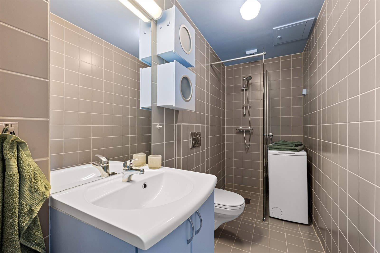 Flislagt baderom med varmekabler i gulv - Badet er fra 2007/2008 og har dusj med sidefelt i glass, servant i helstøpt plate, benkeskap med glatte fronter, veggfestet klosett med innebygget sisterne - Vaskemaskin medfølger Galleribilde