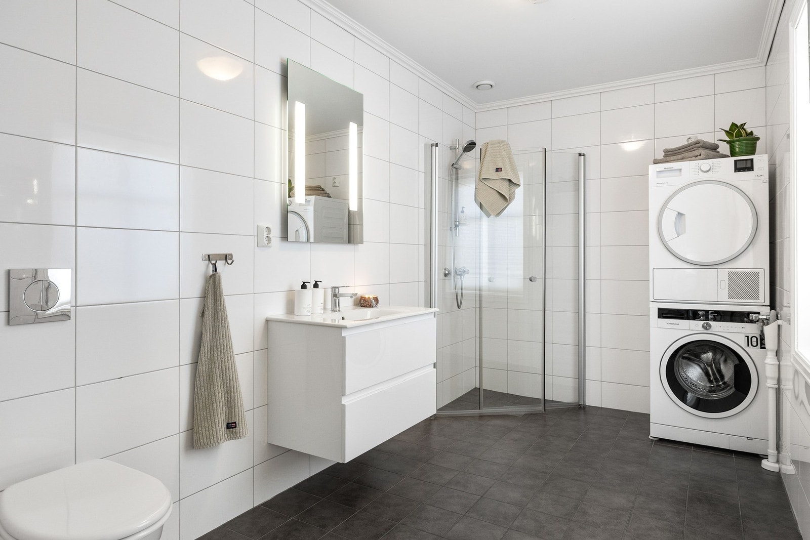 Første etasje har et lyst, flislagt bad med dusjkabinett, vegghengt toalett og opplegg for vaskemaskin/tørketrommel. Galleribilde