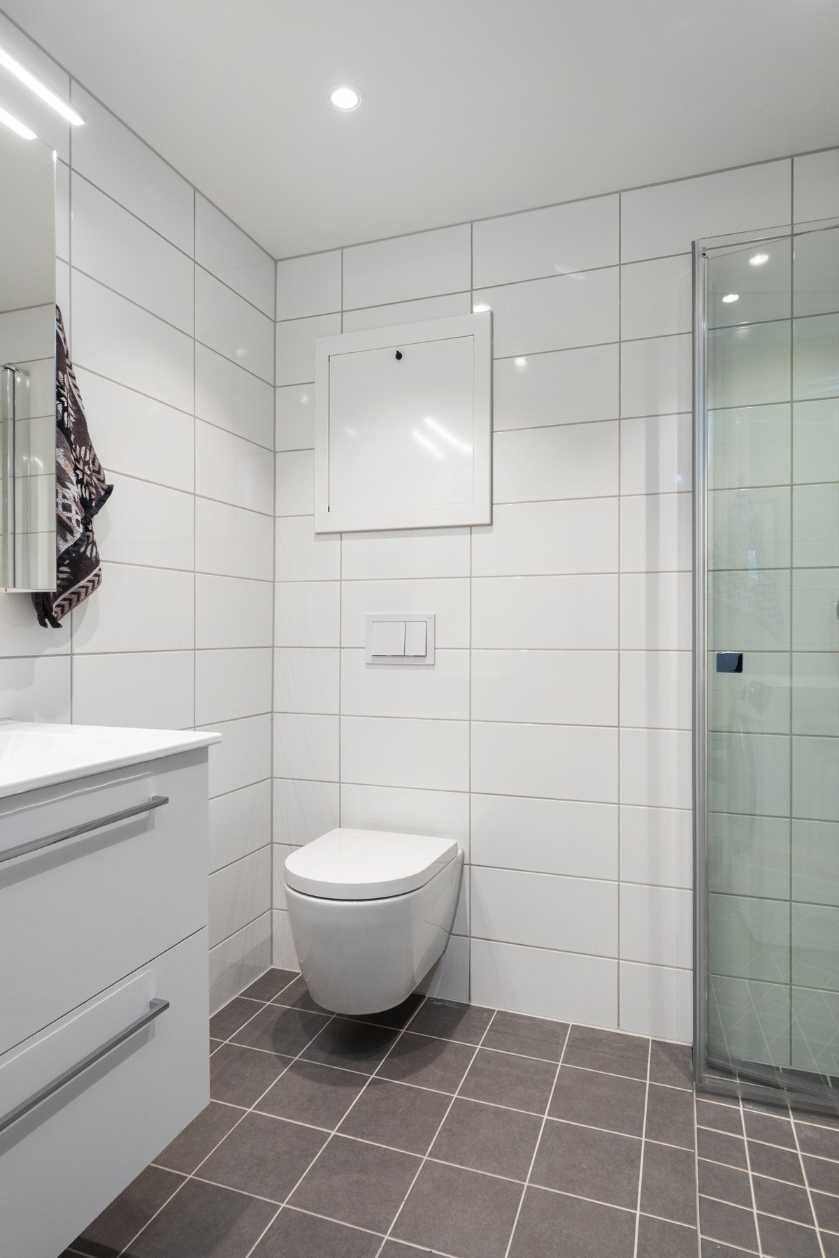 Badet har vegghengt toalett, downlights i taket og et dusjhjørne med innfellbare dører. Galleribilde