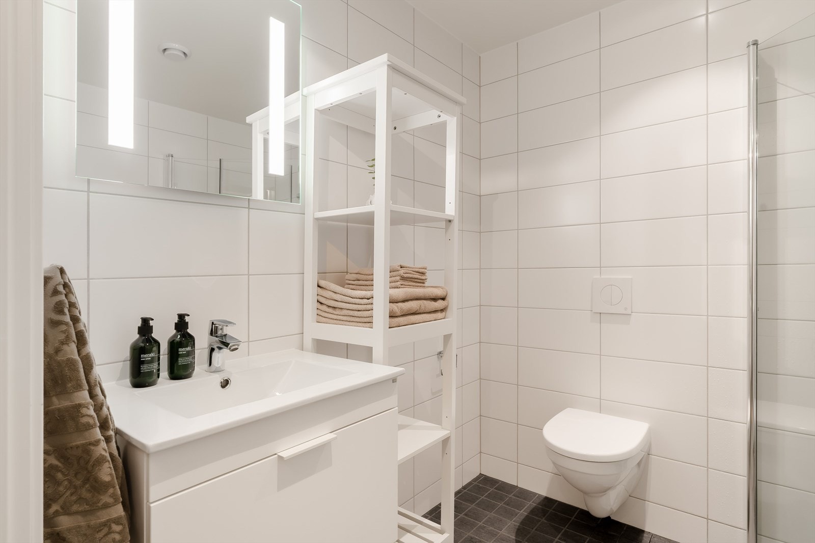 Rommet er innredet med vegghengt toalett, servantinnredning med skuffer, speilskap med integrert belysning, dusjsone med glassvegger og opplegg/plass til vaskemaskin. Galleribilde