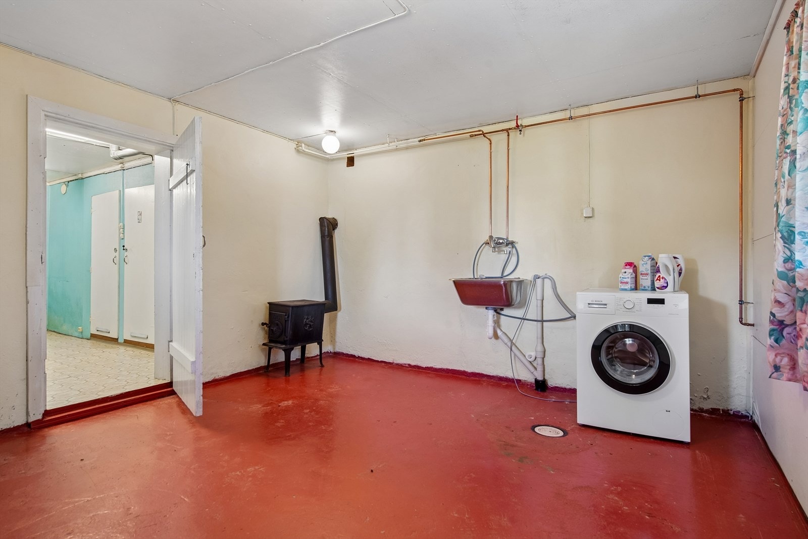 Praktisk vaskekjeller med opplegg for vaskemaskin, utslagsvask og en eldre vedovn. Galleribilde