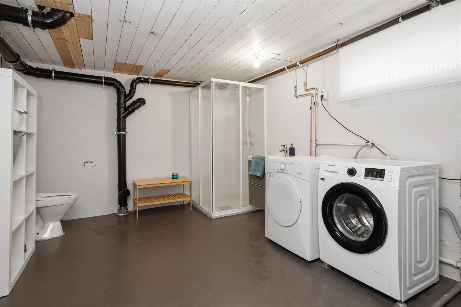 Vaskerom med betonggulv, pussede vegger og panel i tak. Rommet er innredet med opplegg for vaskemaskin, dusjnisje, toalett og varmtvannstank. Galleribilde