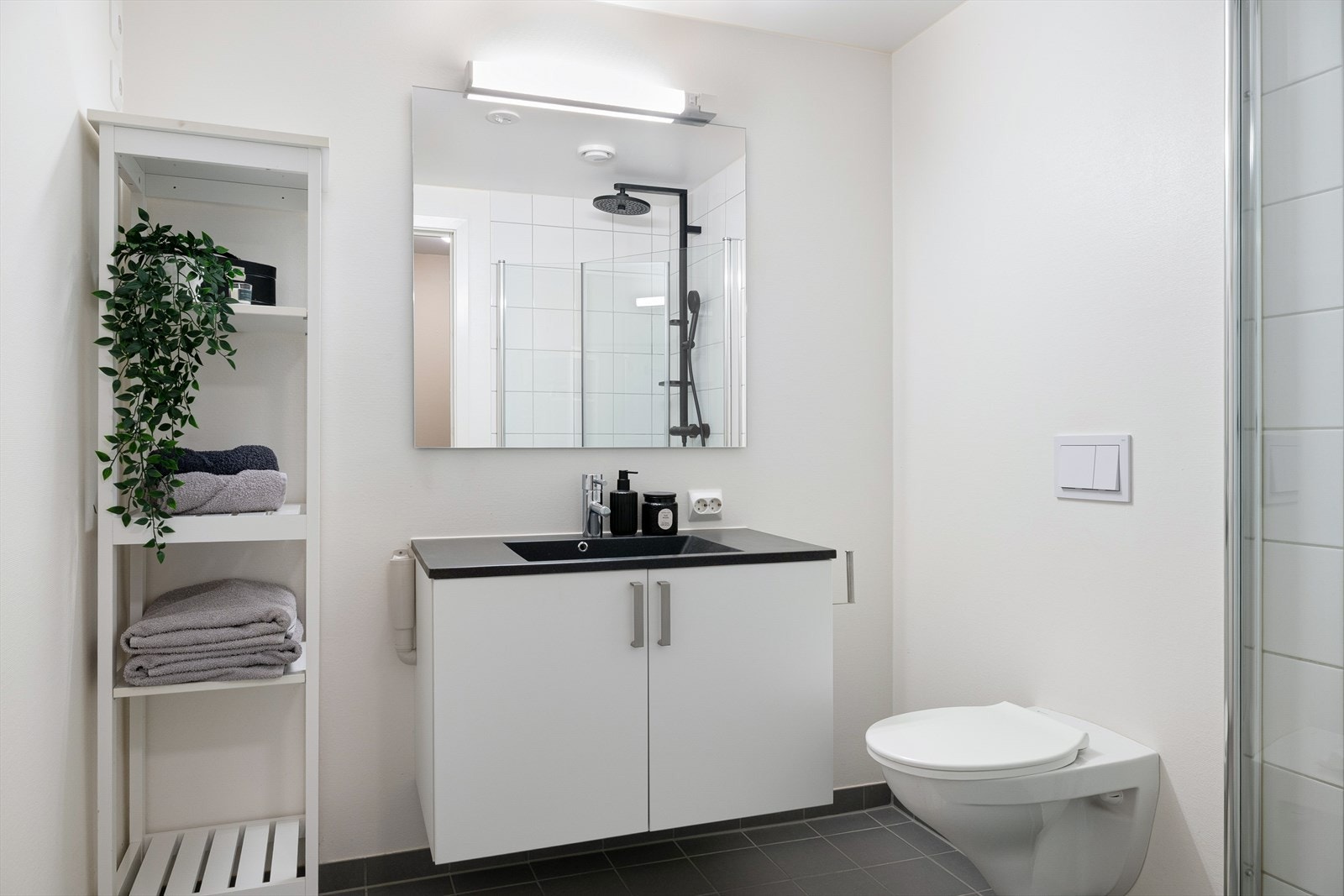 Badet er også lyst og fint med flislagt gulv og vegger i dusjsone. Elektrisk gulvvarme. Det inneholder veggehengt toalett, infellbare dusjvegger i glass og servant med underskap, samt opplegg for vaskemaskin. Galleribilde