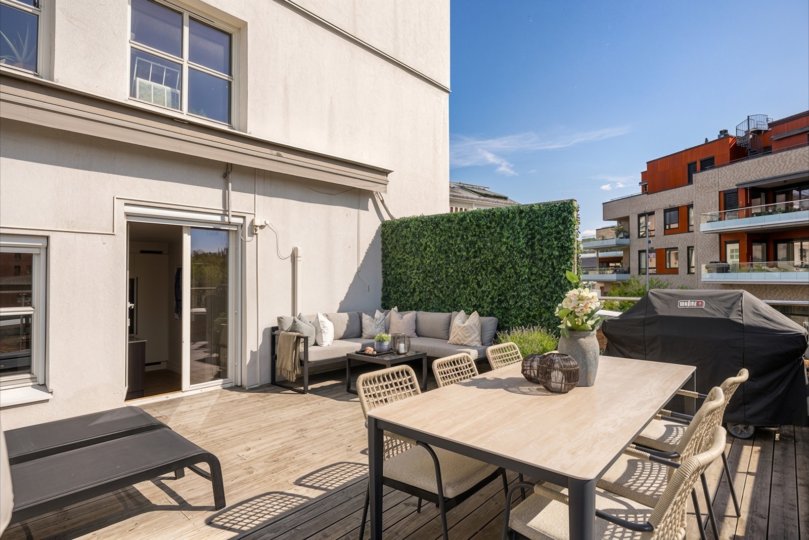 Takterrassen har dekke av terrassebord, rekkverk i glass, samt skjerming fra en grønn levegg på siden og en motorisert markise i overkant. Galleribilde