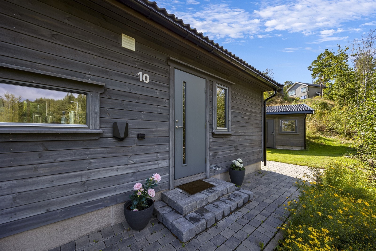 Et velholdt inngangsparti med belegningsstein og elbillader. Galleribilde