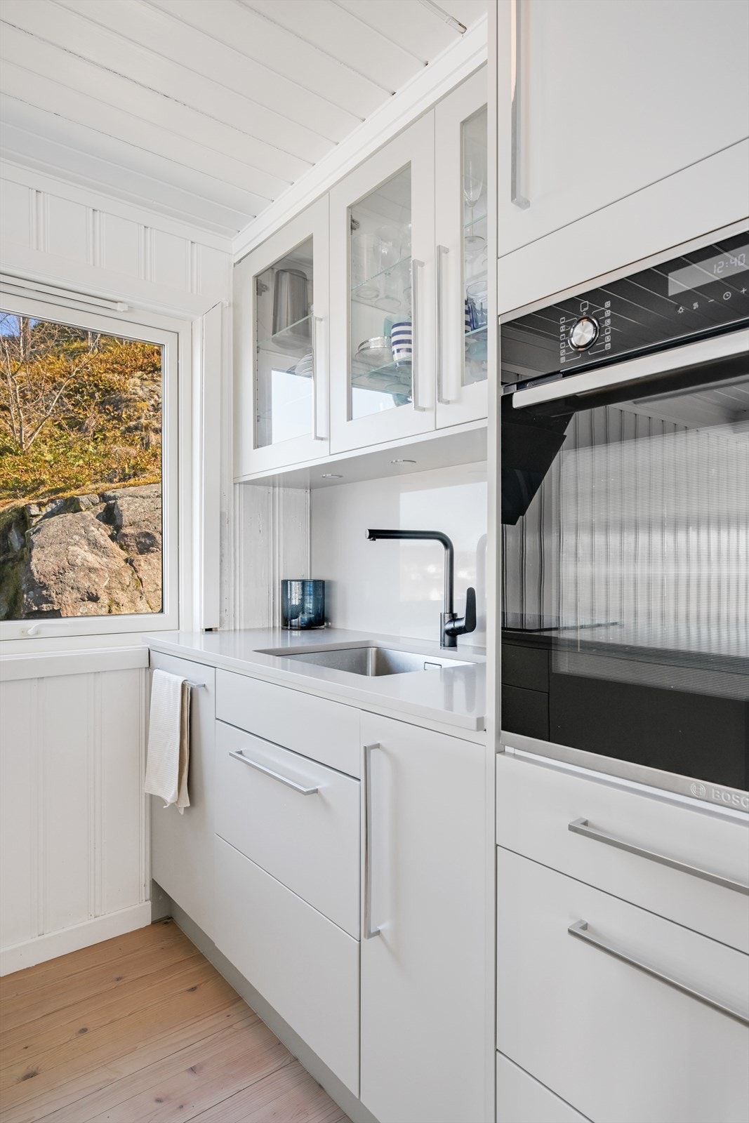 Benkeskapsbelysning under overskap. Nedfelt platetopp og ventilator på vegg, integrert oppvaskmaskin og komfyr i høyskap, samt kjøleskap med frysedel. Galleribilde