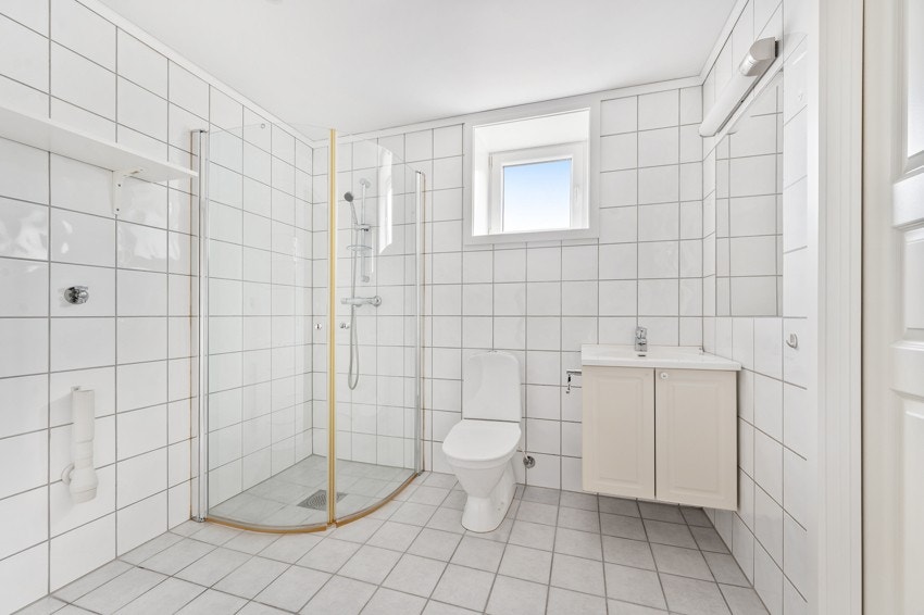 Bad med toalett, servant med oppbevaring, dusjhjørne og opplegg for vaskemaskin. Galleribilde