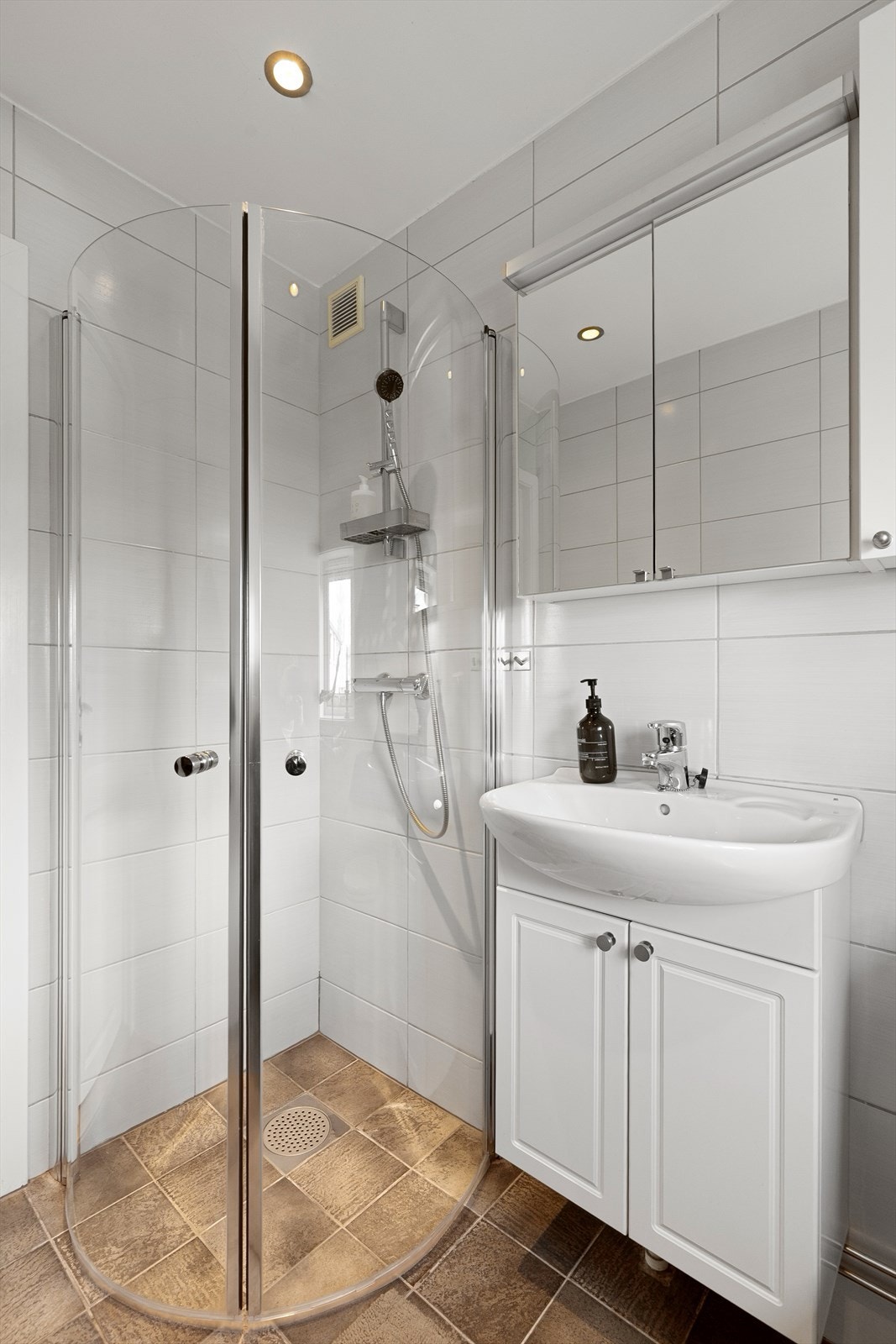 Badet er utstyrt med dusj med innfellbare dører i herdet glass, servant med under- og overskap, og downlights i himling. Galleribilde