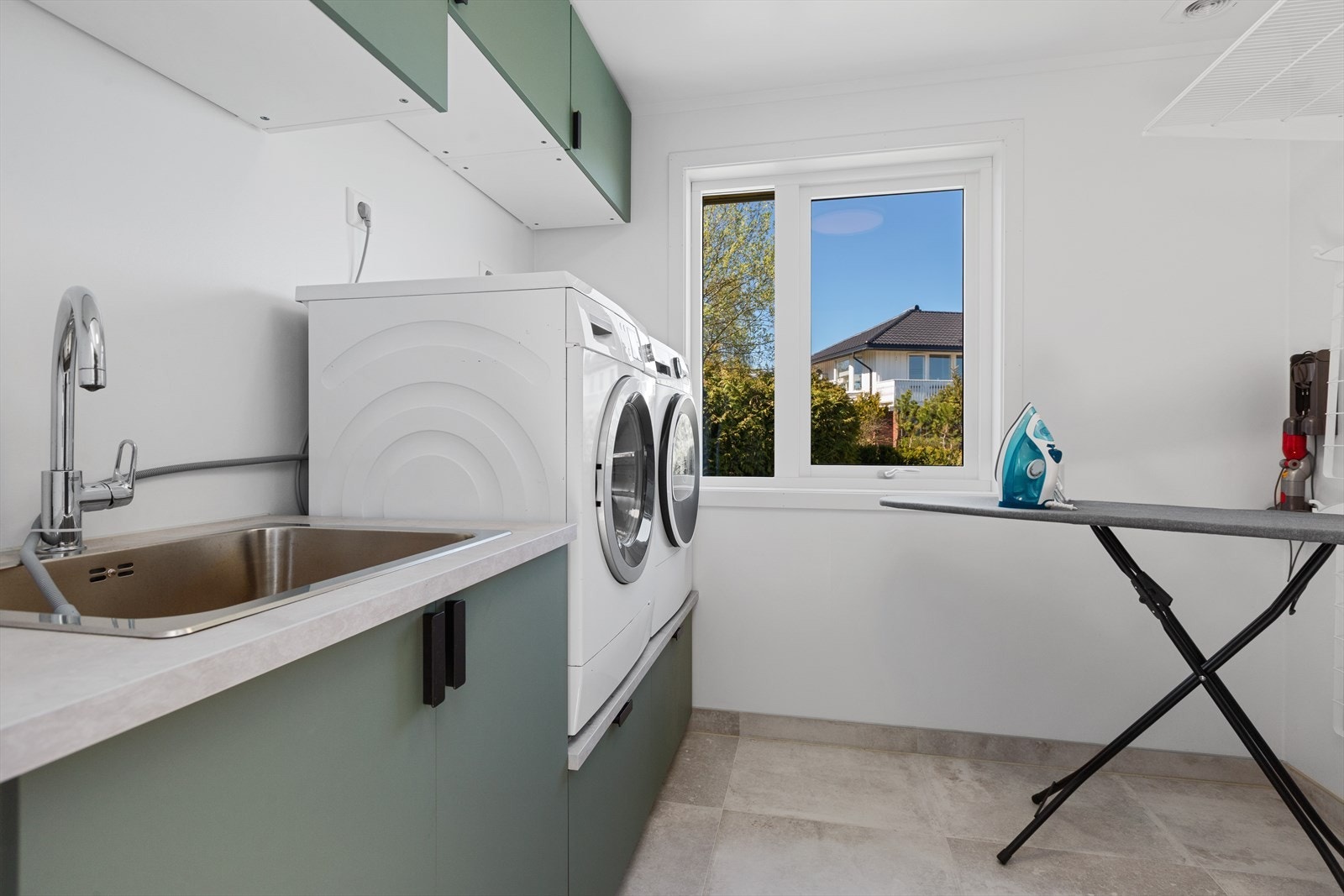 Praktisk vaskerom, oppgradert i 2022 med flislagt gulv med varmekabler. Rommet er utstyrt med innredning som har slette grønne fronter og laminat benkeplate med utslagsvask, samt opplegg for vaskemaskin. Galleribilde