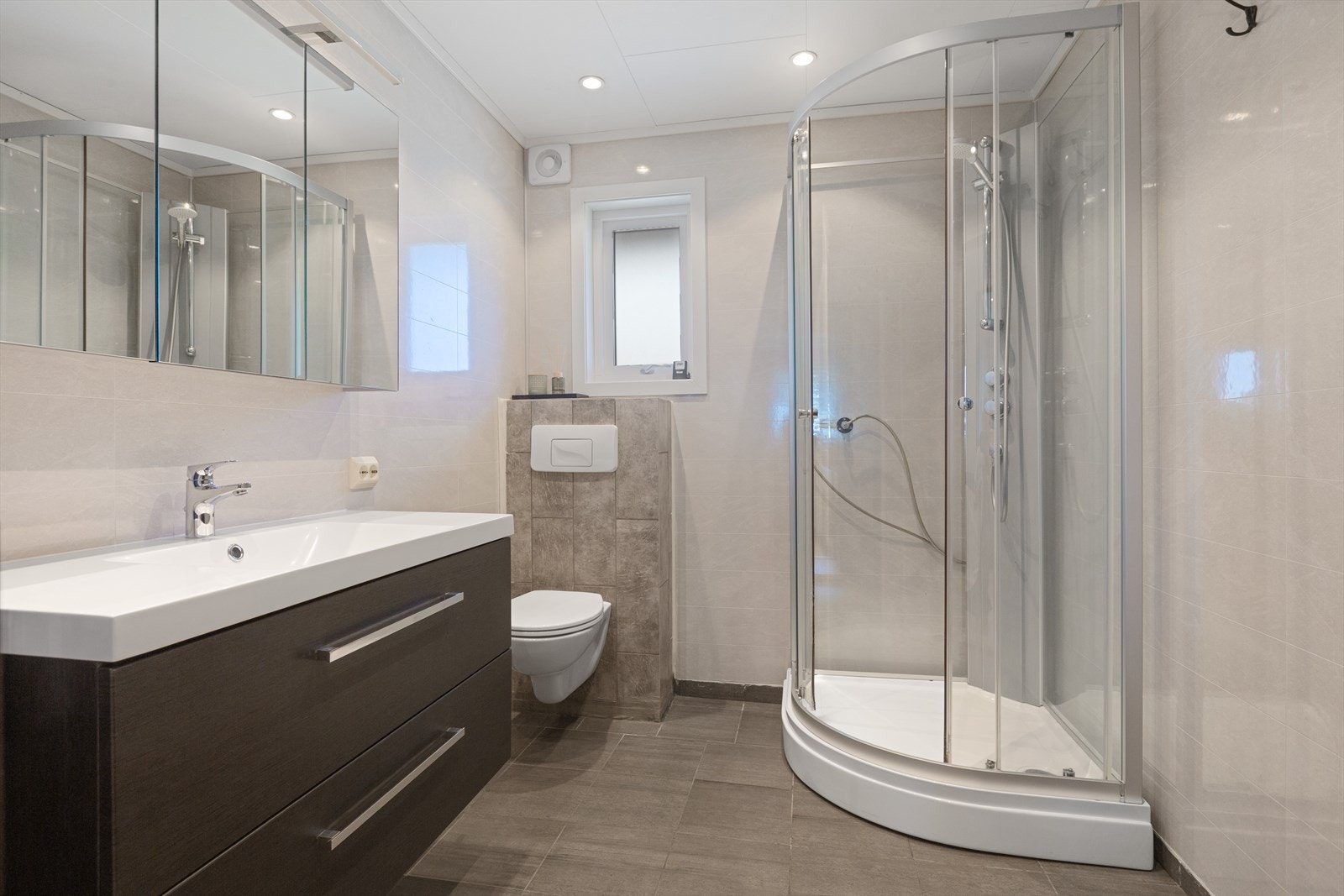 Badet ble renovert i 2018, med flislagt gulv med gulvvarme og baderomsplater på veggene. Rommet er utstyrt med vegghengt toalett, dusjkabinett, samt innredning med servant og speilskap. Galleribilde