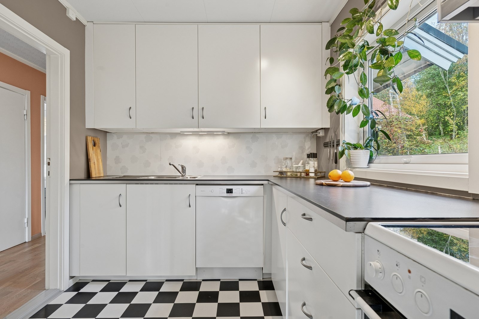 Innredningen (fra 2014) er stilren med hvite slette fronter, benkeplate med nedfelt kjøkkenvask og Backsplashplate over komfyr/vask Galleribilde