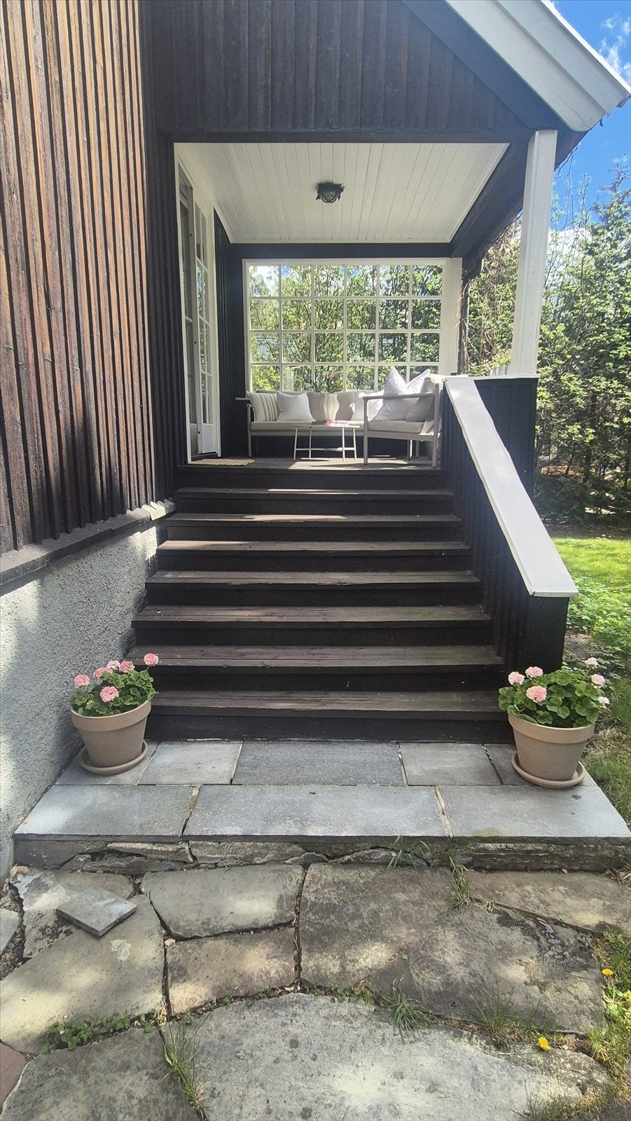 Inngangspartiet har en trapp med dekorative blomster og en overbygd veranda med sitteplass. Galleribilde