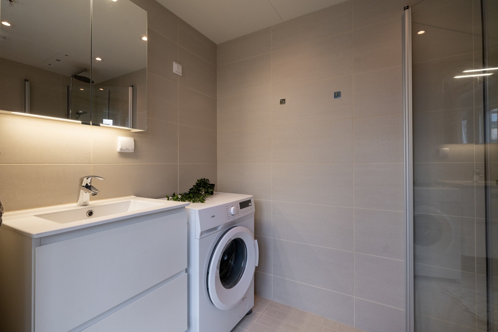 Badet er utstyrt med innredning med skap med glatte fronter og nedfelt servant, veggmontert toalett og regnfalldusj, samt opplegg for vaskemaskin. Galleribilde