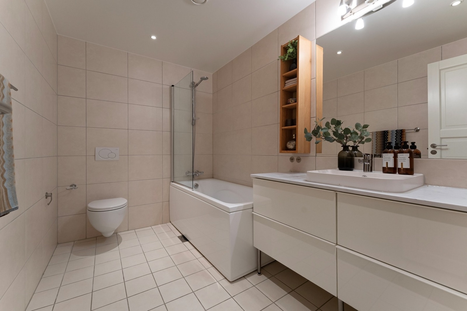 Badet er romslig, og fremstår funksjonelt med flislagte overflater og er innredet med toalett, servant og badekar Galleribilde