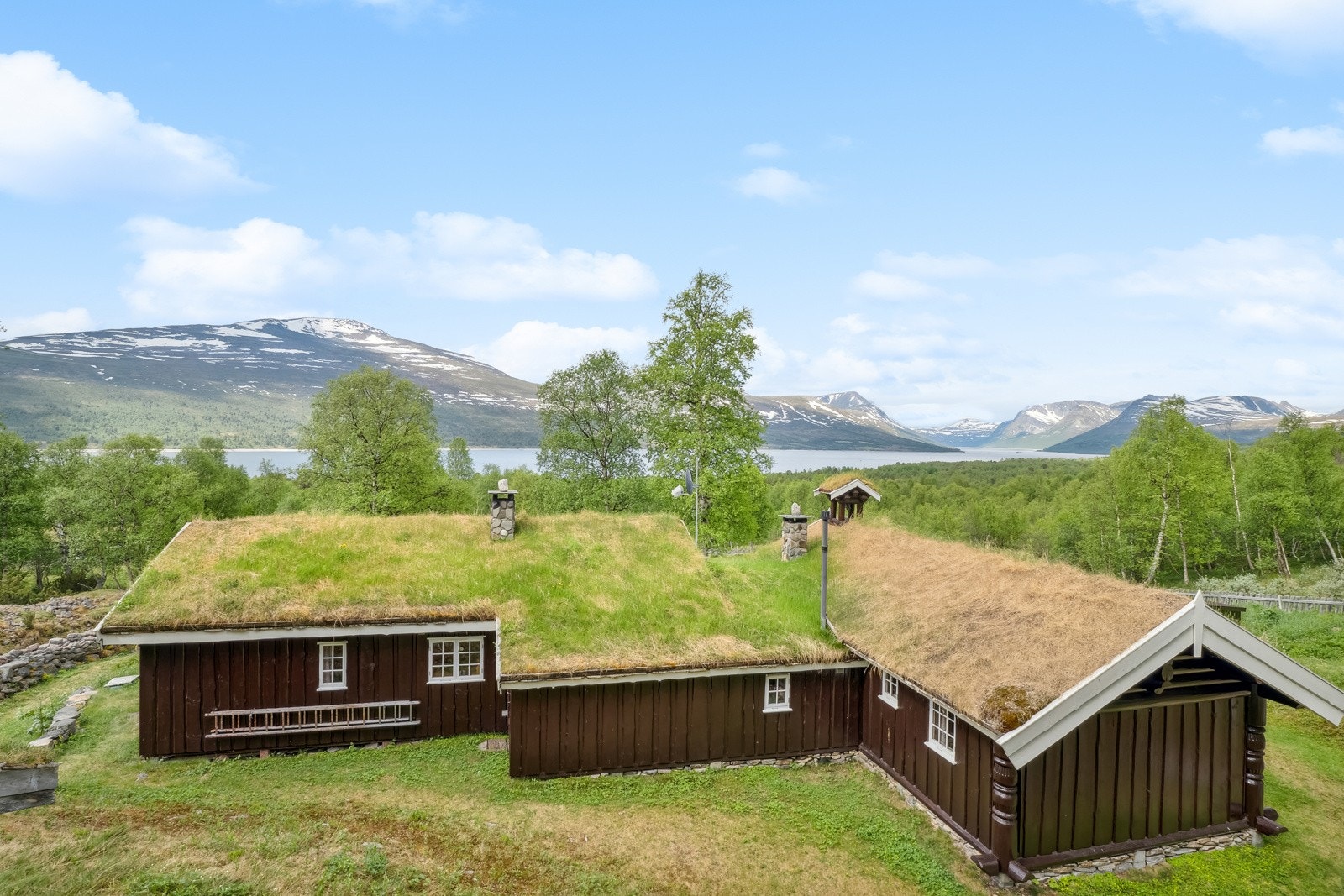 Hytta er perfekt tilpasset tomten og landskapet, med tradisjonelt torvtak, mørk kledning og hvit staffasje. Galleribilde