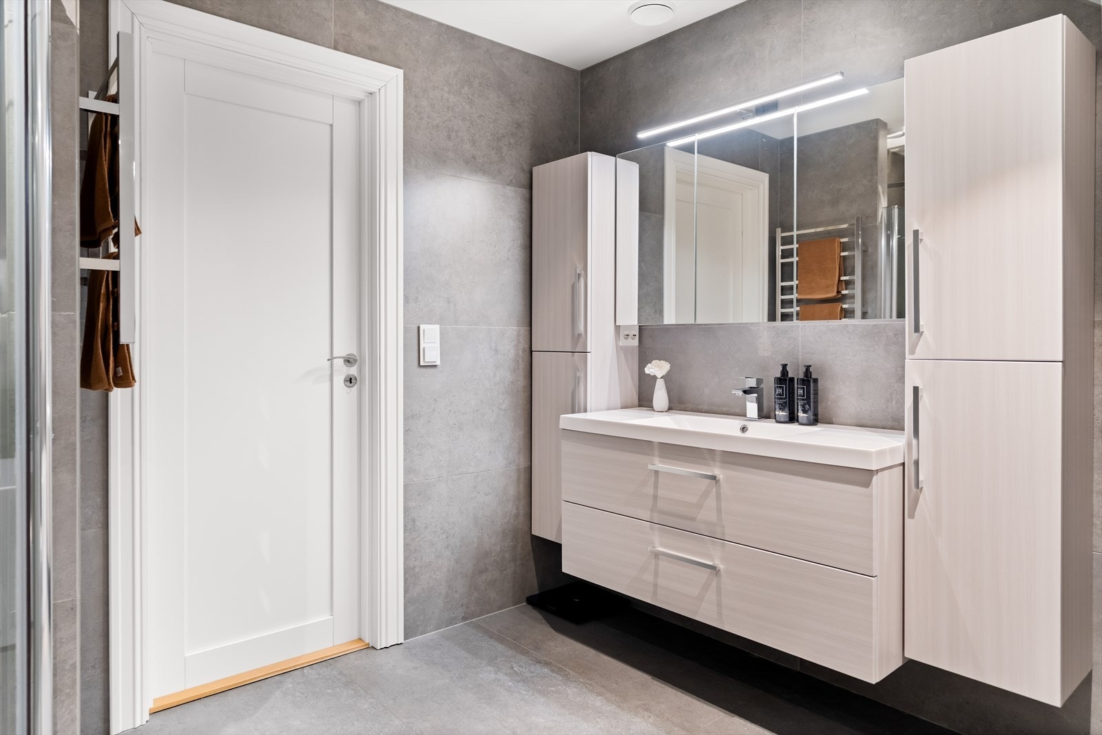 Boligens hoveddel inneholder to bad/wc og et vaskerom. Det største badet ligger ved soverommene i andre etasje, og har downlights i himlingen, store grå fliser på veggene og matchende fliser på gulv med gulvvarme. Galleribilde