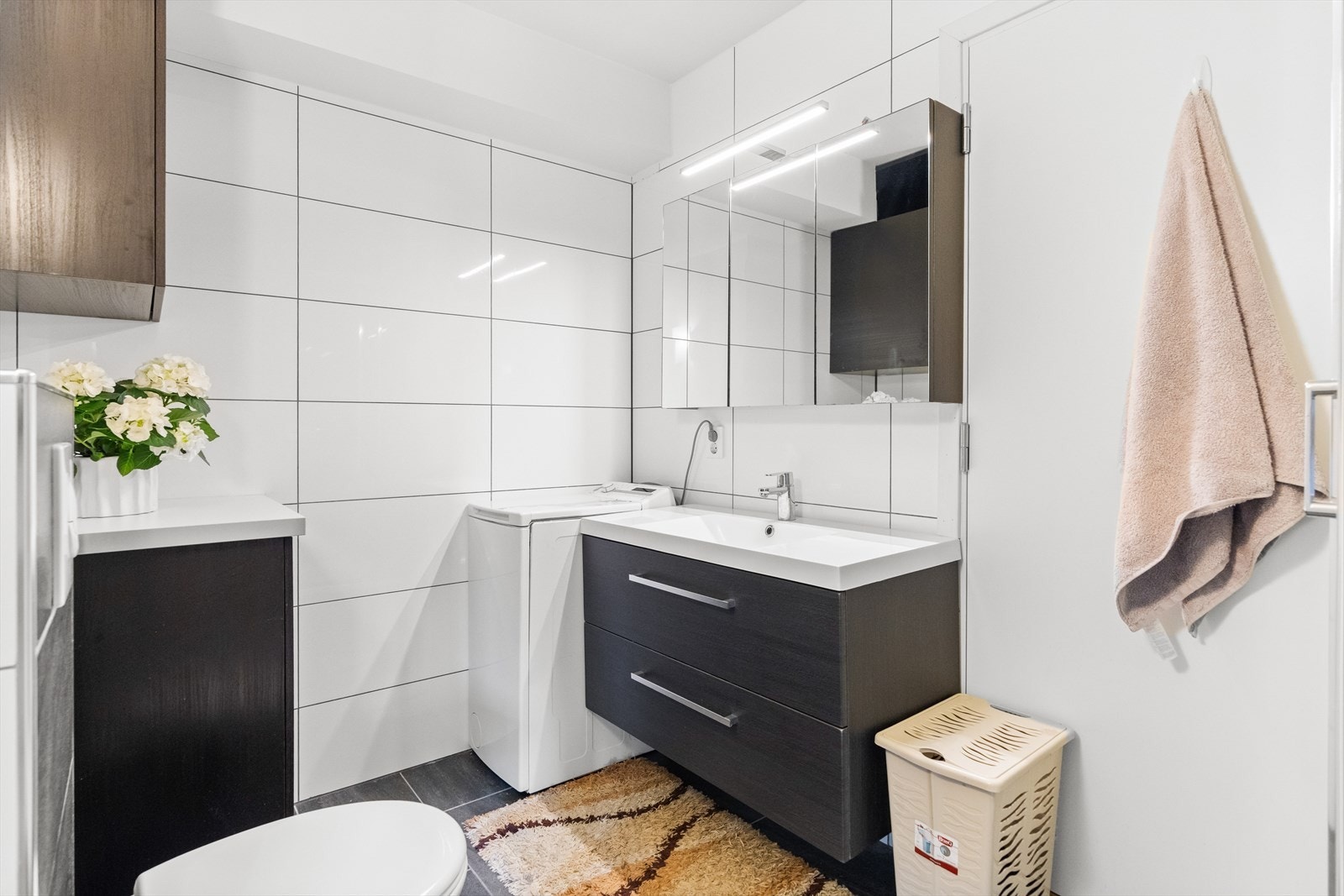 Badet i utleiedelen har hvite fliser på veggene og grå fliser på gulv med gulvvarme. Baderomsinnredningen har mørke, finerte fronter og består av en heldekkende servant på en skuffeseksjon, et sideskap, et veggskap og et bredt speilskap med belysning. Galleribilde