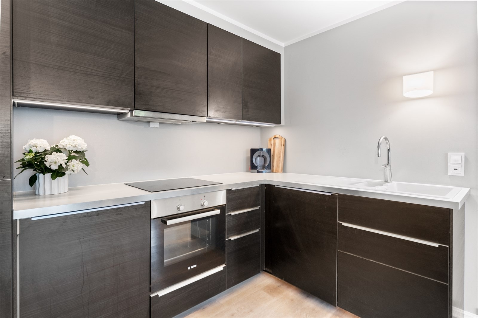 Innredningen fra Ikea har mørke, finerte fronter og hvit benkeplate med hvit, nedfelt kum. Videre er kjøkkenet utstyrt med integrert oppvaskmaskin, kjøl-/fryseskap, stekeovn og koketopp, samt kullfilterventilator, komfyrvakt og god arbeidsbelysning. Galleribilde