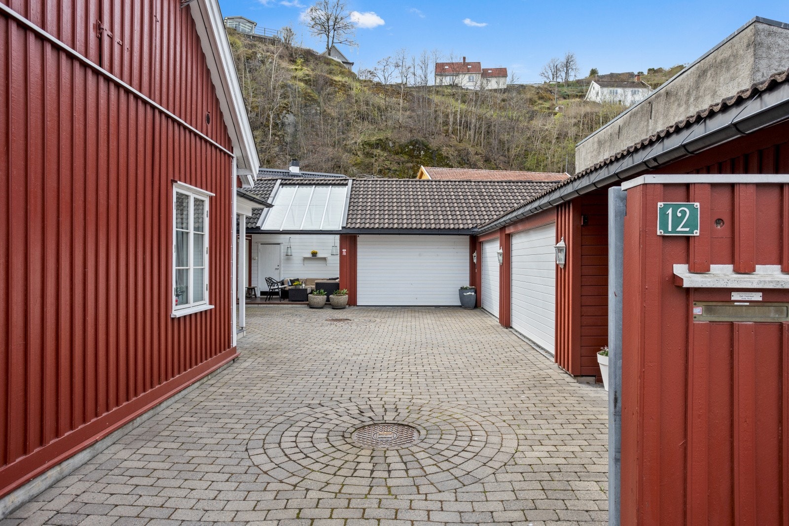 Den romslige, belegningssteinsatte gårdsplassen fremstår som både praktisk og innbydende, og gir enkel og komfortabel adkomst til både boligen og garasjeanlegget. Galleribilde