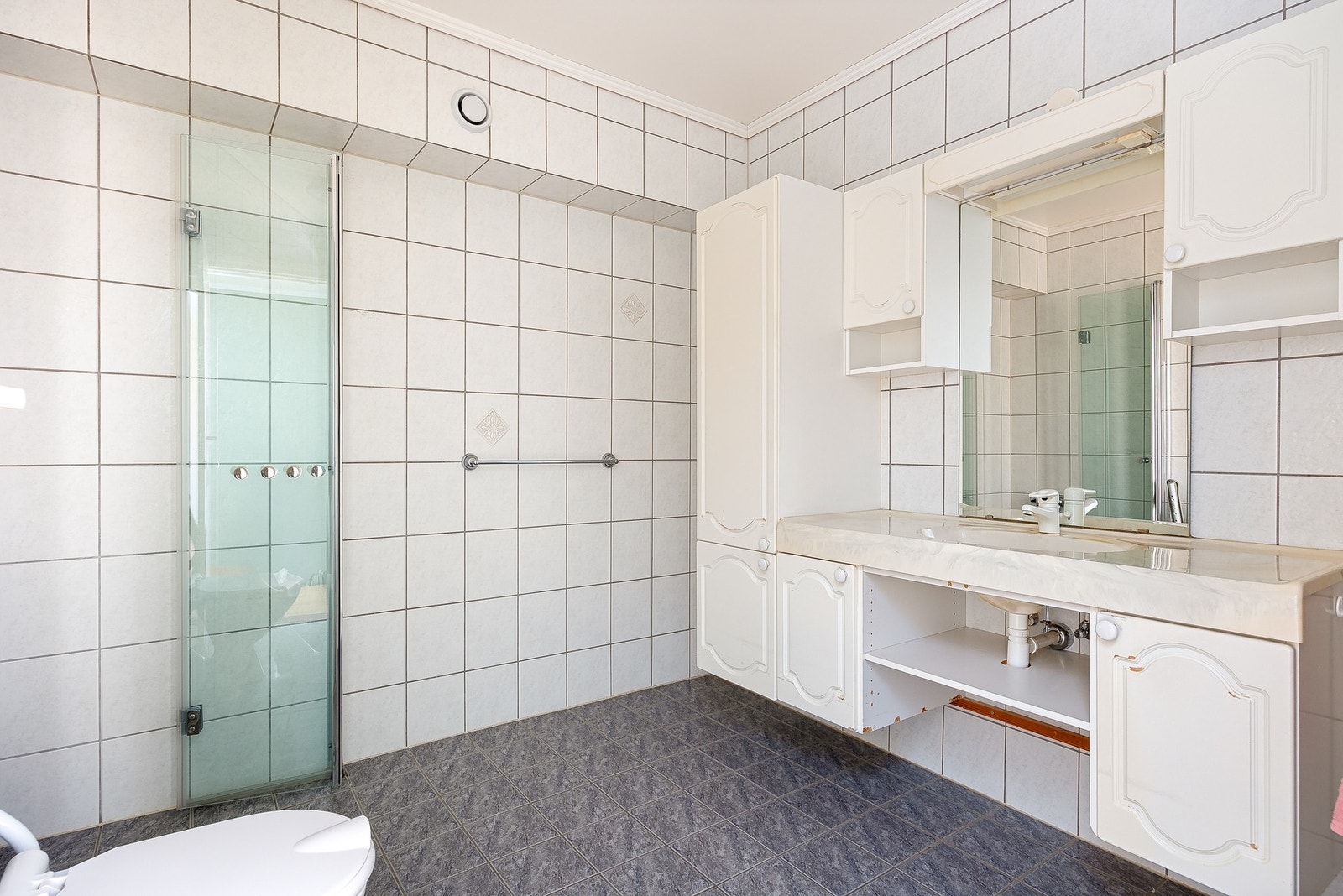 Bad innredet med servantmøblement med speil, toalett og dusj. Modernisering av badet bør påregnes Galleribilde
