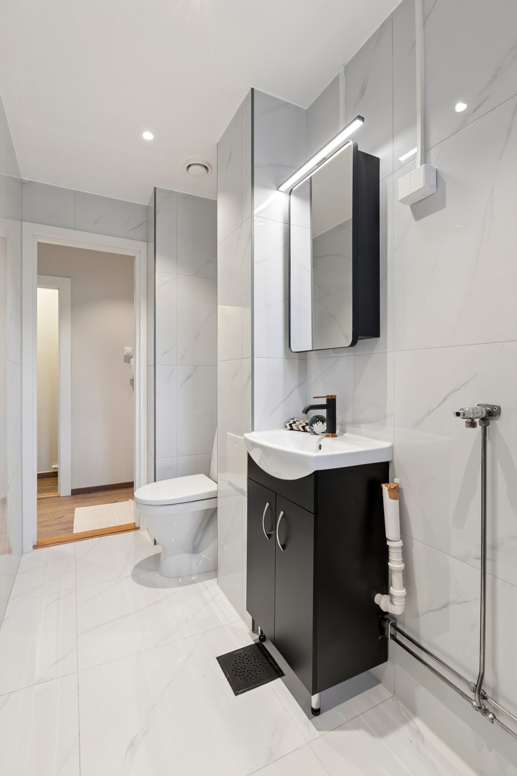 Servantinnredning med sorte, glatte fronter, speil med LED-belysning og ettgreps armatur. Galleribilde