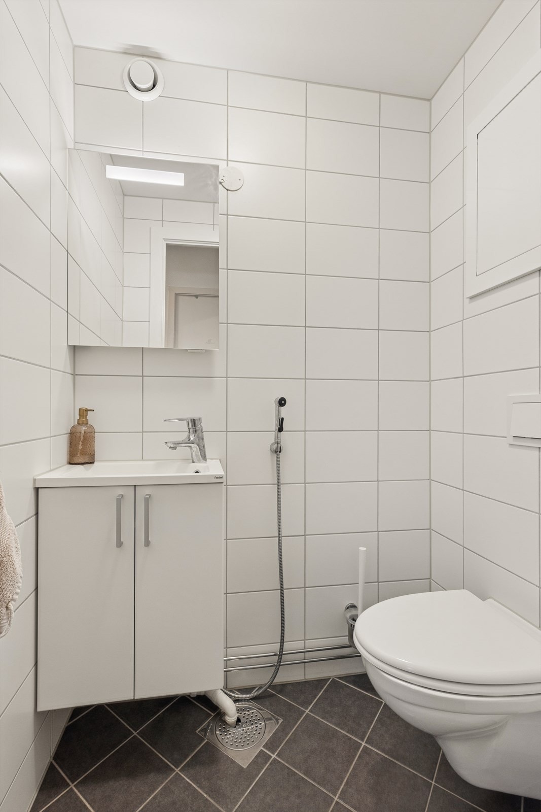 Praktisk separat toalettrom med flislagte overflater, vegghengt toalett og servantinnredning. Galleribilde