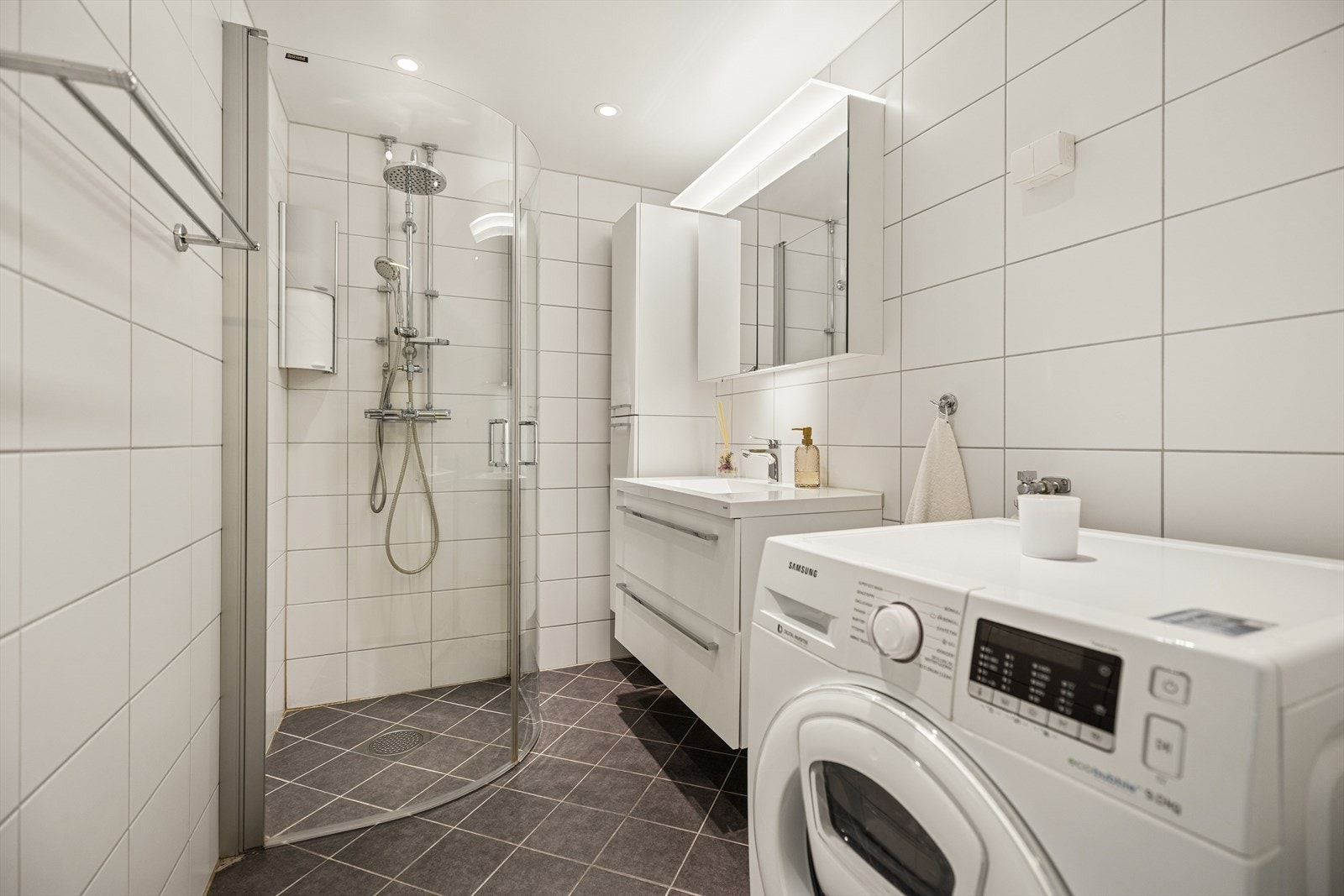 Badet har en praktisk utforming med dusjhjørne, servantinnredning og opplegg for vaskemaskin. Galleribilde