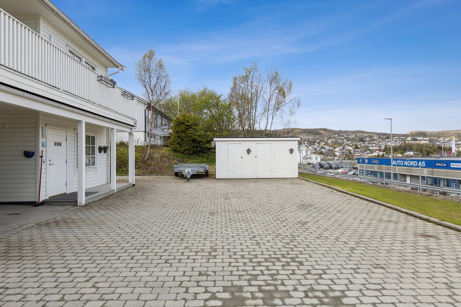 Fasade med steinlagt gårdsplass, støttemurer og egen carport. Utebod er felles med nabo i dag. Galleribilde