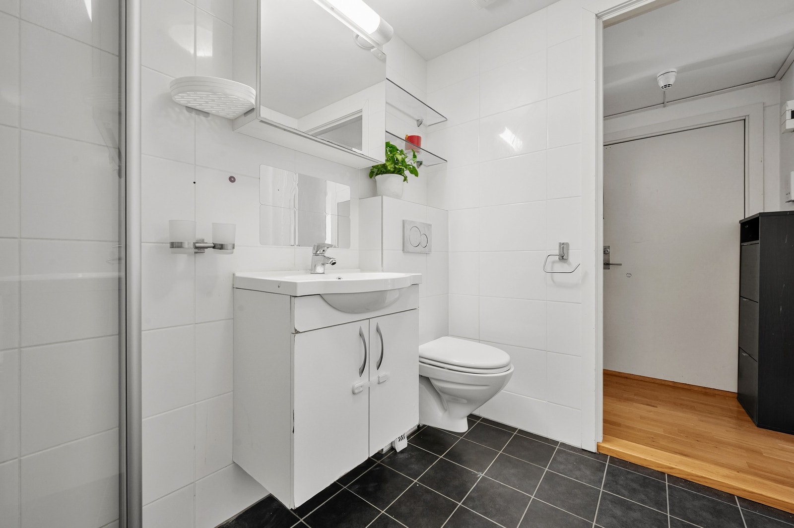 Innredningen består av servantinnredning, speil i dører på overskap på vegg over servant, vegghengt toalett, dusjhjørne med svingbare glassdører og opplegg for vaskemaskin. Galleribilde