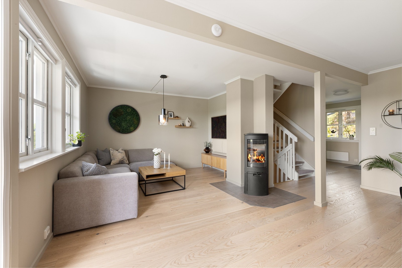 Planløsningen gir god plass til både sofagruppe og spisebord, perfekt for både hverdagsliv og sosiale sammenkomster. Mellom sonene står en stilfull peisovn med glass på tre sider - et naturlig samlingspunkt som tilfører både varme og atmosfære i vinterhal Galleribilde