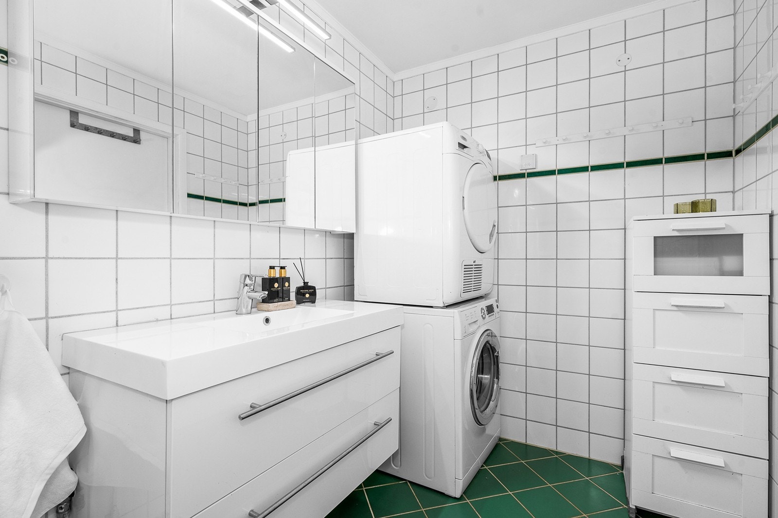 Flislagt bad med varmekabler i gulvet og en praktisk planløsning. Badet er innredet med heldekkende servant på underskap, speilskap med belysning og dusjkabinett. Galleribilde