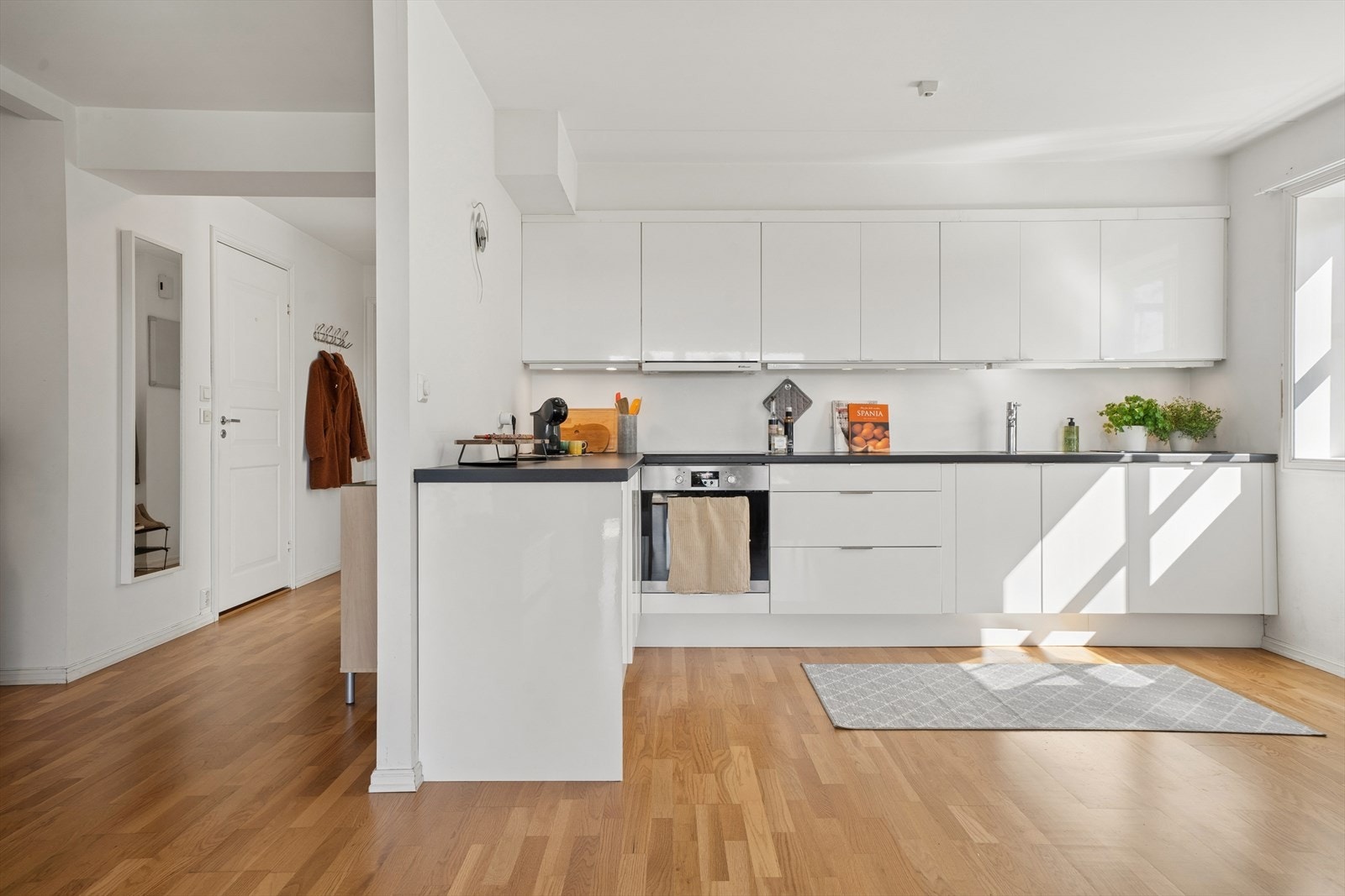 Leiligheten har en åpen stue- og kjøkkenløsning med gjennomgående parkettgulv. Kjøkkeninnredningen fra Ikea har hvite høyglansfronter og integrerte hvitevarer. Galleribilde