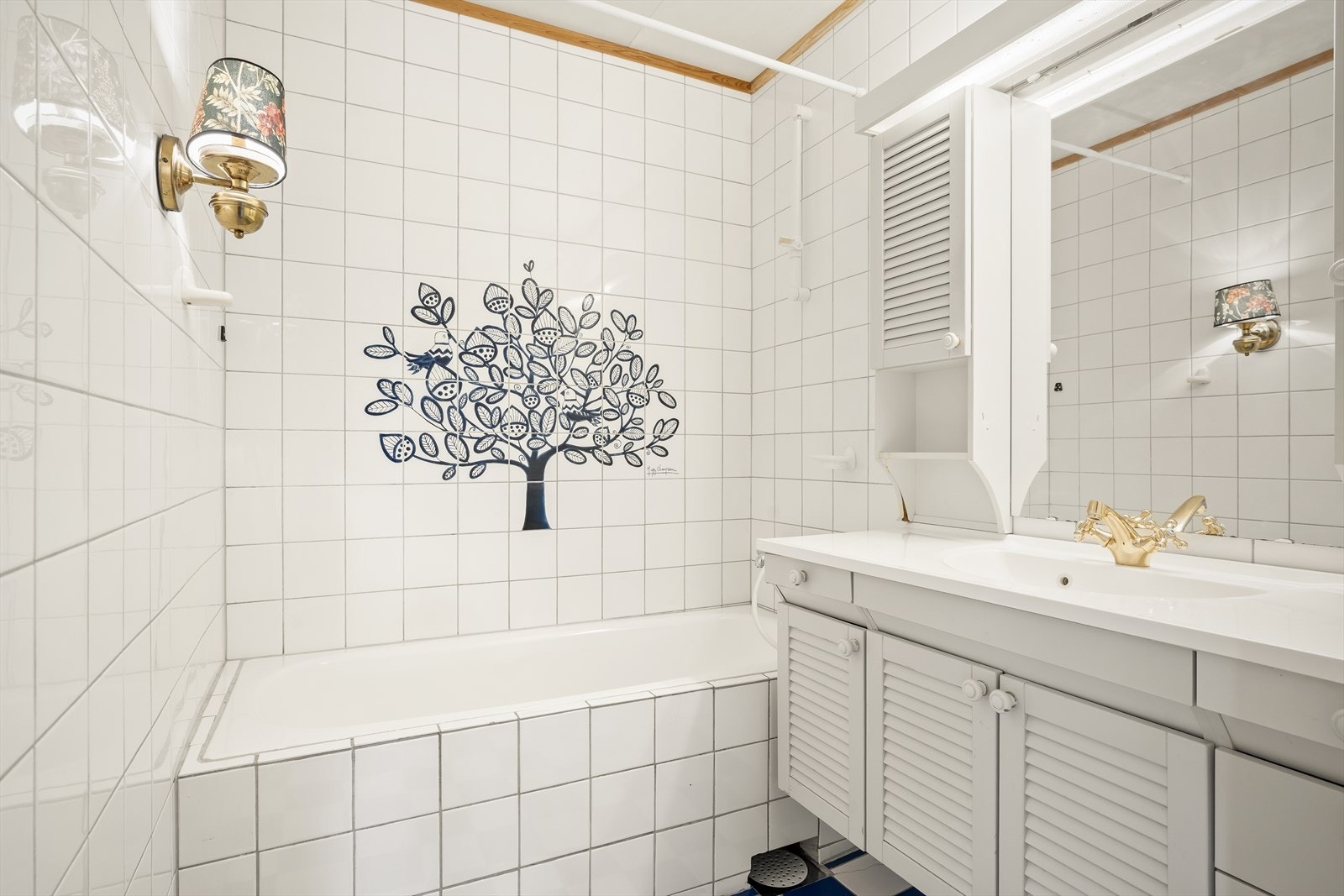 Eldre bad med flislagte overflater på gulv og vegger. Badet ligger i tilkytning til hàllen. Galleribilde