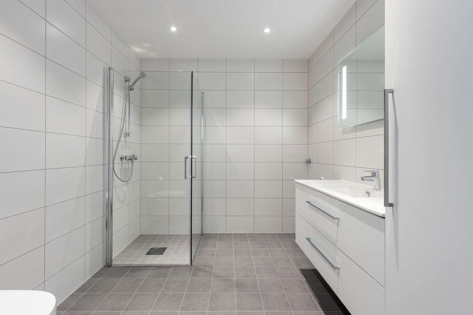 Pent bad som er innredet med baderomsinnredning med vask, speil og høyskap, toalett, dusjnisje med innfellbare glassdører, samt opplegg for vaskemaskin. Galleribilde